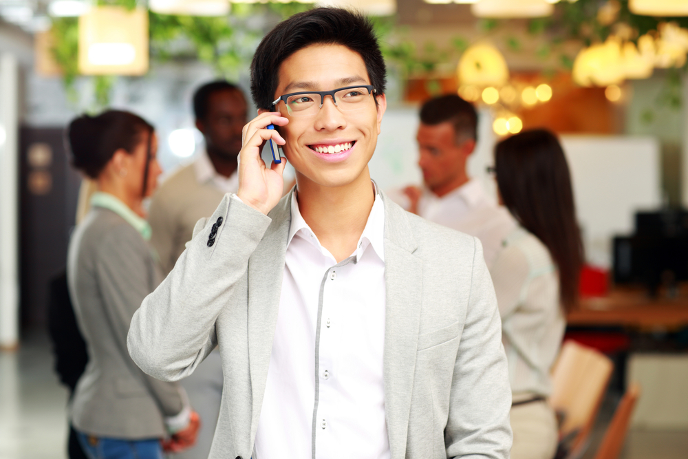 Portrait of a smiling businessman talking on the smartphone in front of colleagues